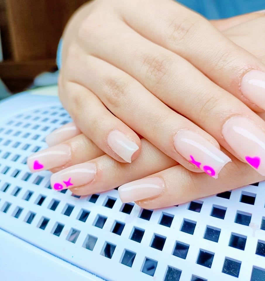 Lichte manicure met kleine roze hartjes op de nageltoppen